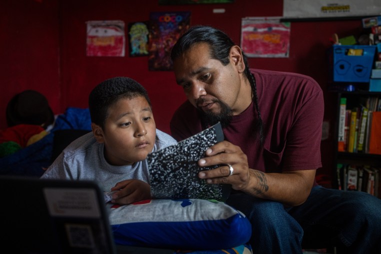 Evan Torres looks at a journal with Robert while seated on a bed