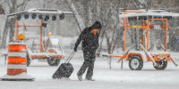 A person walks through the snow with a suitcase as snow falls