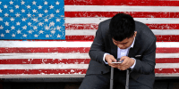 In this April 10, 2018, photo, a man on a bench with an American flag checks his smartphone in Beijing.